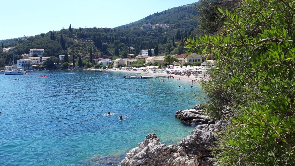 View of Kalami Beach in Corfu, Greece. A crowded peddle beach with sunbeds and clear waters.
